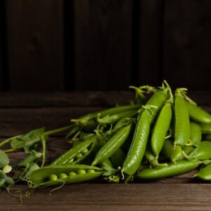 Herneitä (500g) vihreinä palkoina puupöydällä.