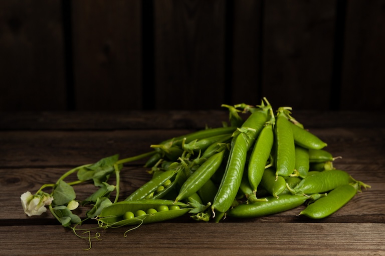 Herneitä (500g) vihreinä palkoina puupöydällä.